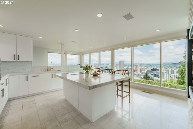 kitchen featuring sink, a kitchen island, tasteful backsplash, a breakfast bar area, and white cabinets