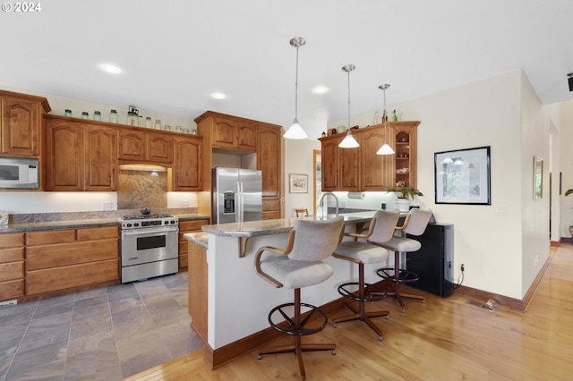 kitchen with hanging light fixtures, stainless steel appliances, a breakfast bar, light stone countertops, and light hardwood / wood-style floors