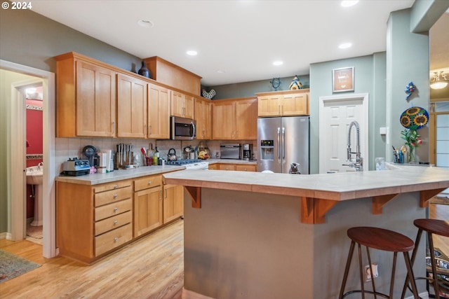 kitchen featuring a kitchen breakfast bar, light wood-type flooring, tasteful backsplash, stainless steel appliances, and light brown cabinets