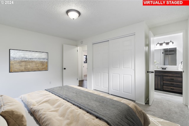 bedroom featuring a textured ceiling, ensuite bathroom, a closet, and light colored carpet