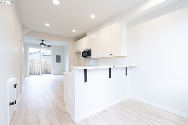 kitchen with a breakfast bar, white cabinets, light hardwood / wood-style flooring, ceiling fan, and kitchen peninsula