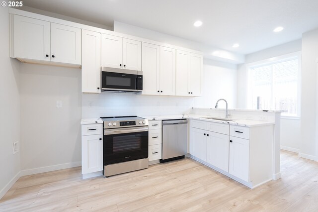 kitchen with white cabinets, appliances with stainless steel finishes, light wood-type flooring, and sink