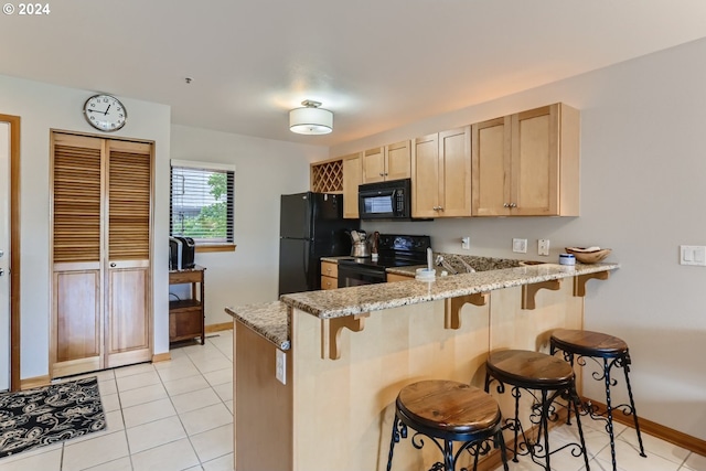 kitchen featuring light stone counters, kitchen peninsula, a kitchen bar, black appliances, and light brown cabinets