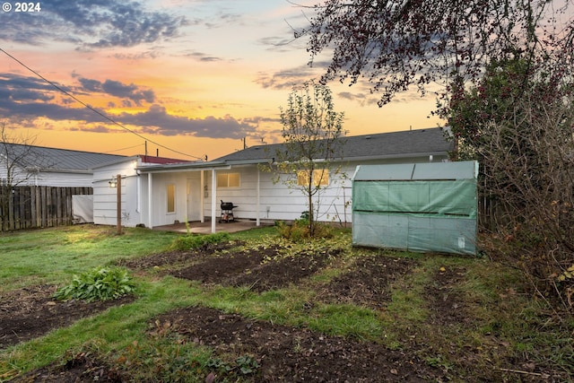 back house at dusk with an outdoor structure, a patio area, and a lawn