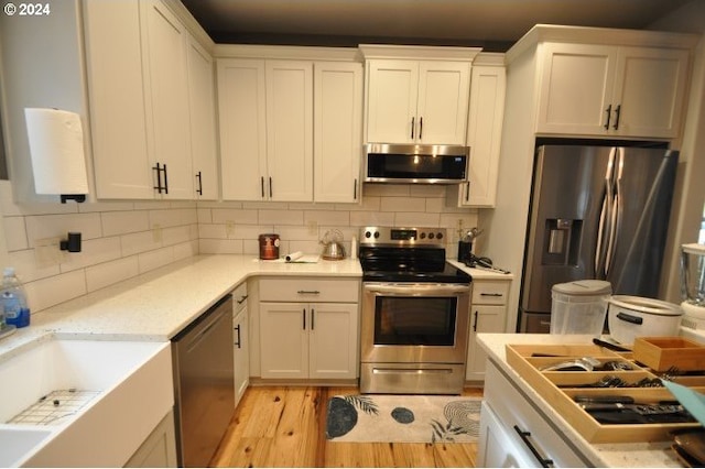 kitchen featuring white cabinets, sink, decorative backsplash, light wood-type flooring, and appliances with stainless steel finishes