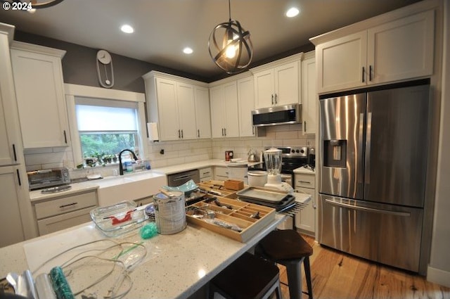 kitchen with white cabinetry, hanging light fixtures, light hardwood / wood-style floors, decorative backsplash, and appliances with stainless steel finishes