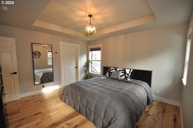 bedroom with a chandelier, light wood-type flooring, and a tray ceiling