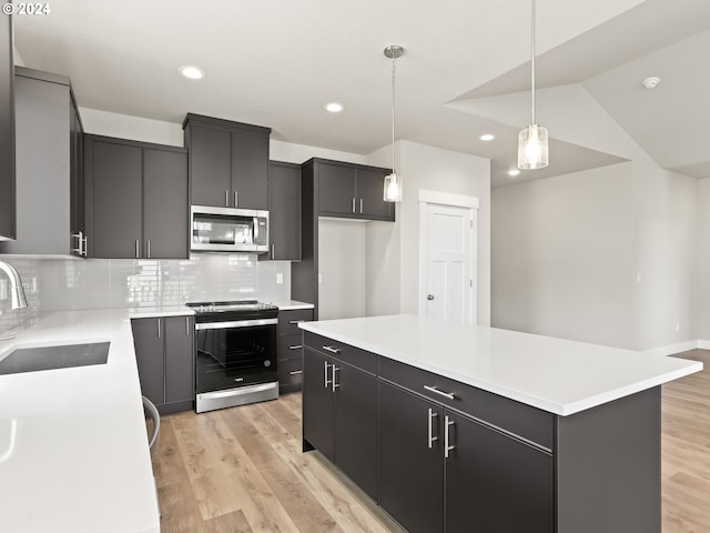 kitchen featuring a kitchen island, stainless steel appliances, sink, hanging light fixtures, and light hardwood / wood-style flooring