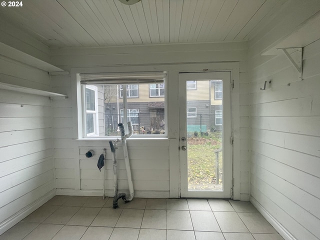 doorway with wooden walls, light tile patterned flooring, and a healthy amount of sunlight