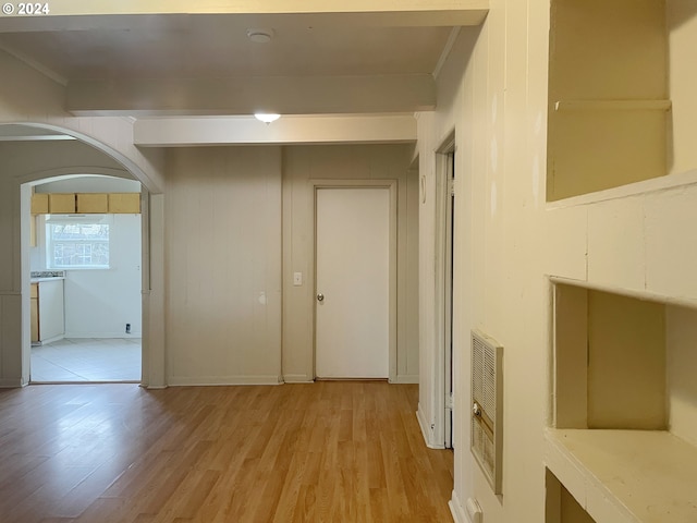 hallway featuring heating unit, crown molding, light hardwood / wood-style flooring, and wooden walls