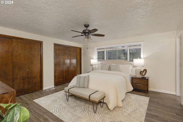 bedroom featuring a textured ceiling, dark hardwood / wood-style flooring, ceiling fan, and multiple closets