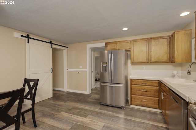 kitchen featuring sink, dark hardwood / wood-style floors, a barn door, a textured ceiling, and appliances with stainless steel finishes