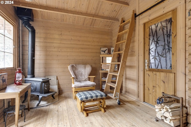 sitting room featuring a wood stove, light hardwood / wood-style flooring, beamed ceiling, and wooden ceiling