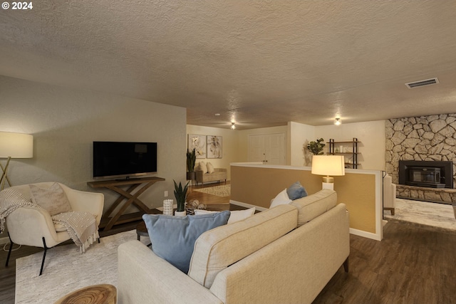 living room with a textured ceiling, a stone fireplace, and dark wood-type flooring