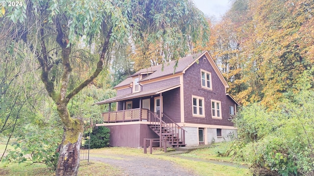 view of front facade featuring stairs, a forest view, a porch, and a shingled roof
