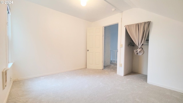 unfurnished bedroom featuring light colored carpet, lofted ceiling, and baseboards
