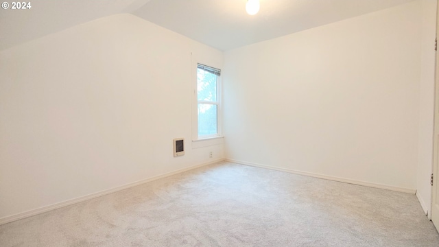 empty room with light carpet, lofted ceiling, and heating unit