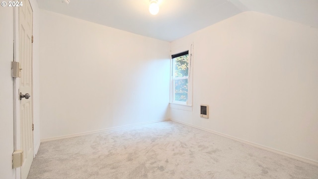 spare room featuring lofted ceiling, light colored carpet, and heating unit