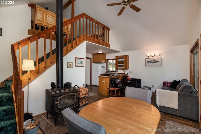 dining room with dark hardwood / wood-style floors, high vaulted ceiling, a wood stove, sink, and ceiling fan