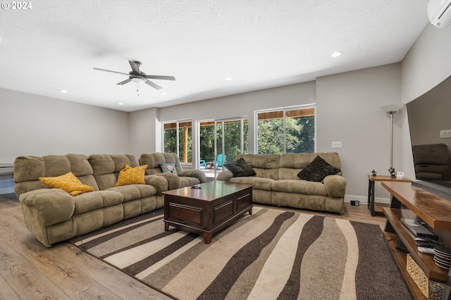 living room with ceiling fan, a wall unit AC, a textured ceiling, and light hardwood / wood-style floors