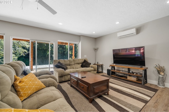 living room with ceiling fan, a textured ceiling, a wall unit AC, and light hardwood / wood-style floors