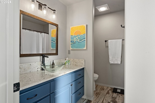 full bath with toilet, baseboards, wood finished floors, and vanity