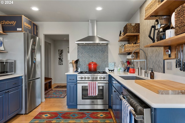 kitchen with wall chimney range hood, blue cabinetry, stainless steel appliances, and light countertops