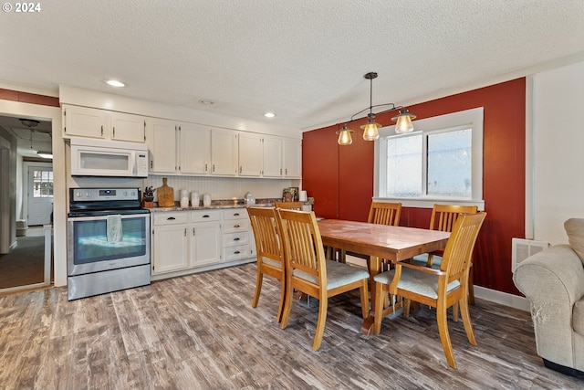 kitchen featuring wood-type flooring, a textured ceiling, decorative light fixtures, stainless steel range with electric stovetop, and white cabinets