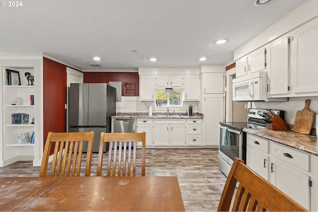 kitchen featuring white cabinetry, light stone counters, a textured ceiling, appliances with stainless steel finishes, and light wood-type flooring