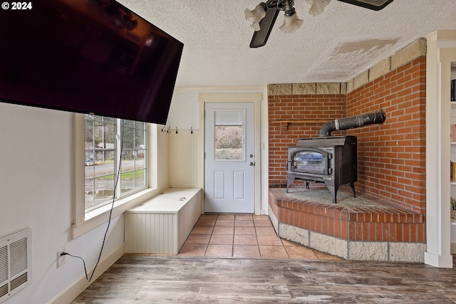 interior space featuring a wood stove, ceiling fan, a textured ceiling, light hardwood / wood-style floors, and brick wall