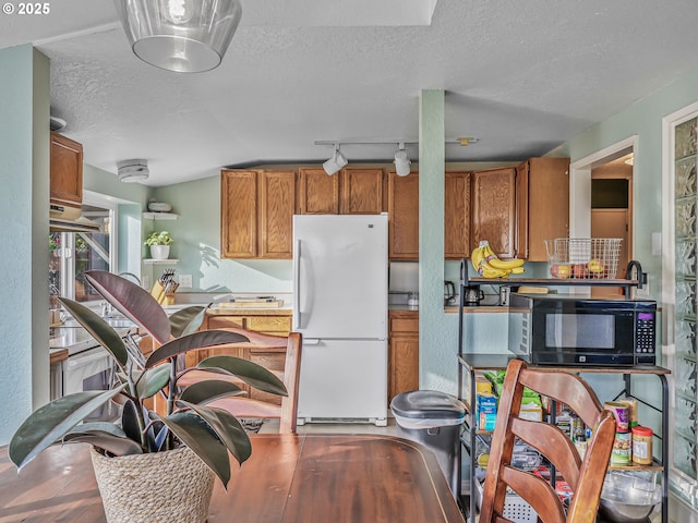 740 Florence Ave, Astoria, OR 97103 - kitchen with freestanding refrigerator, black microwave, brown cabinetry, a textured ceiling, and track lighting