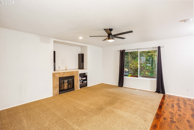 unfurnished living room with hardwood / wood-style floors, a tiled fireplace, and ceiling fan