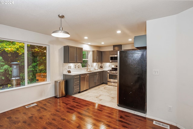 kitchen with backsplash, appliances with stainless steel finishes, pendant lighting, sink, and light hardwood / wood-style floors