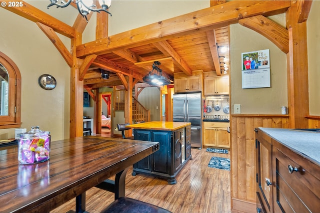 kitchen with light brown cabinets, light hardwood / wood-style flooring, stainless steel fridge, a kitchen island, and wood walls