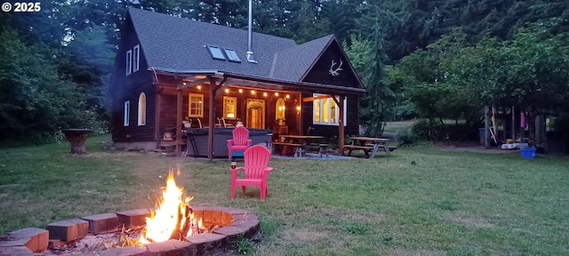 rear view of house with an outdoor fire pit, a lawn, and a hot tub