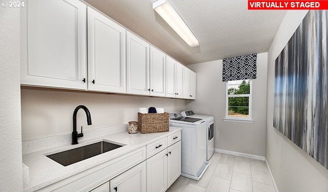 clothes washing area with sink, washer and dryer, a textured ceiling, and cabinets