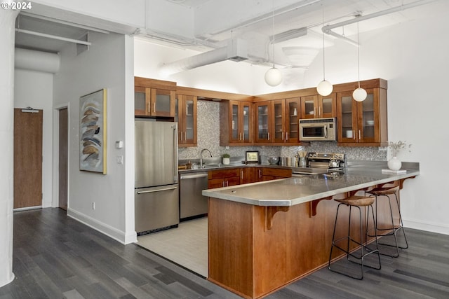 kitchen featuring tasteful backsplash, a peninsula, a kitchen breakfast bar, brown cabinetry, and stainless steel appliances