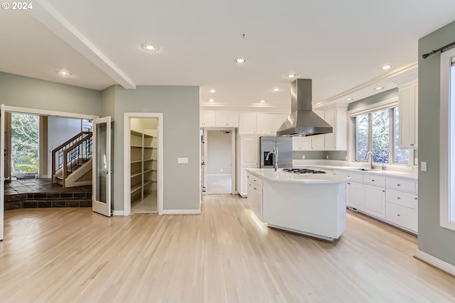 kitchen with an island with sink, sink, wall chimney range hood, white cabinetry, and light wood-type flooring