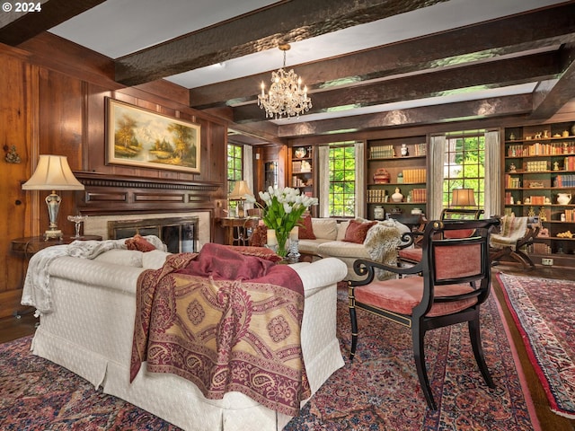 living room with beamed ceiling, a notable chandelier, a healthy amount of sunlight, wooden walls, and built in features