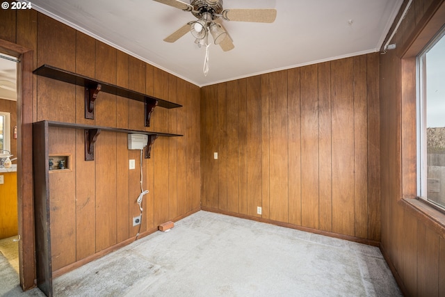 carpeted empty room featuring a healthy amount of sunlight, crown molding, and wood walls