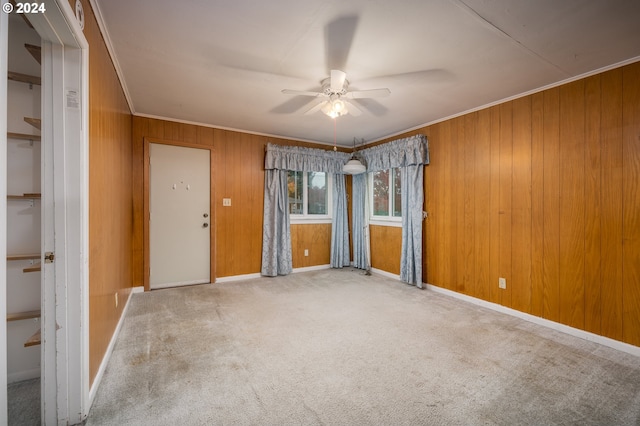 unfurnished room featuring carpet, wooden walls, ceiling fan, and crown molding