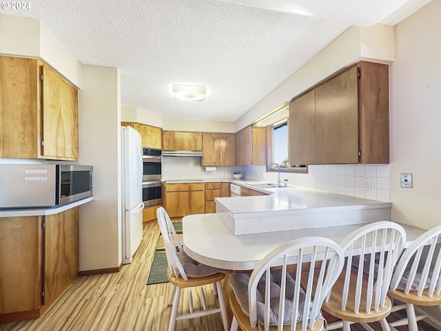 kitchen with kitchen peninsula, decorative backsplash, light hardwood / wood-style floors, and stainless steel appliances