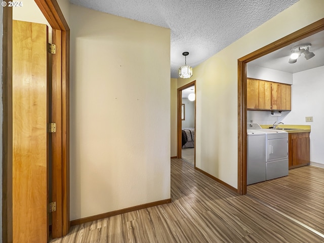 hallway with a textured ceiling, wood-type flooring, sink, and washing machine and clothes dryer