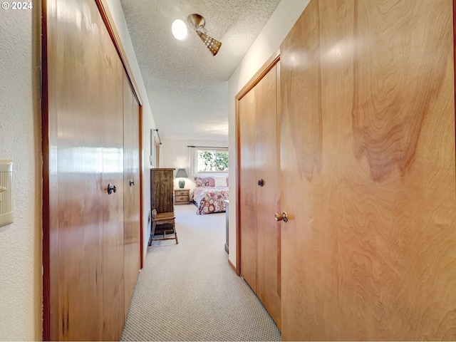 corridor with light colored carpet and a textured ceiling