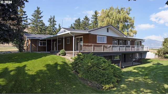 rear view of property featuring a mountain view, a balcony, and a yard