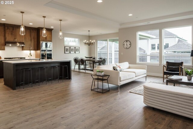 living room with a raised ceiling, a stone fireplace, and light wood-type flooring