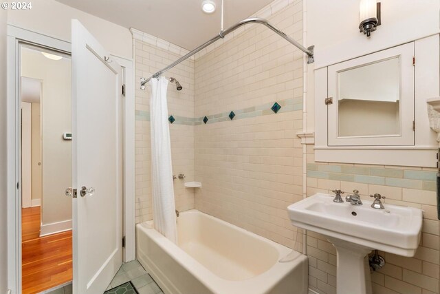 bathroom featuring wood-type flooring, shower / tub combo with curtain, and tile walls