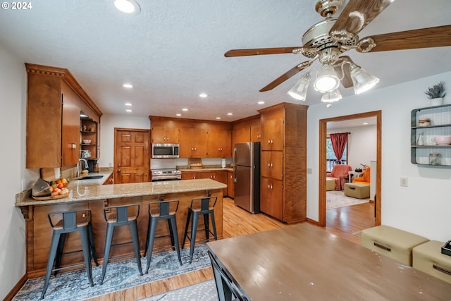 kitchen with kitchen peninsula, sink, stainless steel appliances, and light hardwood / wood-style flooring