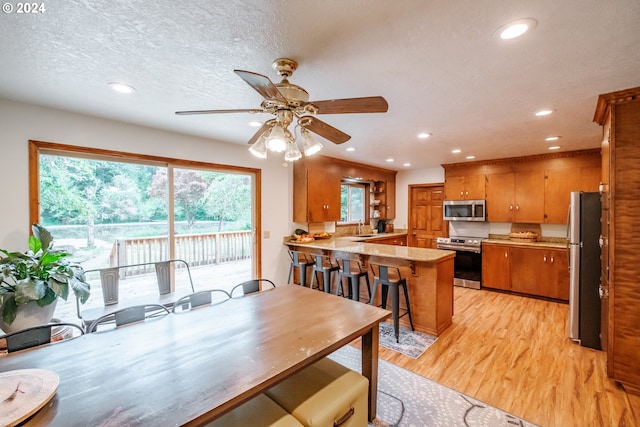 dining area featuring ceiling fan, sink, a textured ceiling, and light hardwood / wood-style flooring