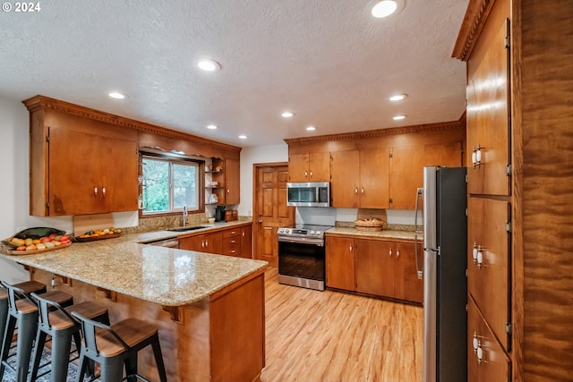 kitchen with sink, light hardwood / wood-style flooring, a textured ceiling, kitchen peninsula, and stainless steel appliances